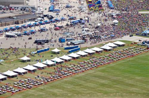 Aerial view of a large outdoor event with tents, crowds, and food trucks on a grassy field.