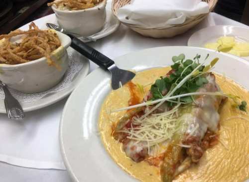 A plate of enchiladas topped with cheese and microgreens, served with a side of crispy onions and butter.
