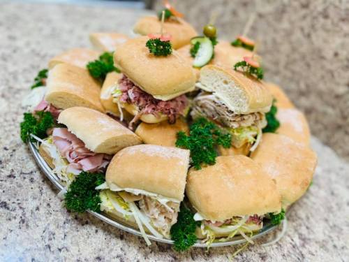 A platter of assorted sandwiches with various fillings, garnished with parsley and pickles, on a textured surface.