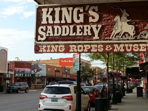 Sign for King's Saddlery with a cowboy on a horse, featuring shops and a street view in a small town.