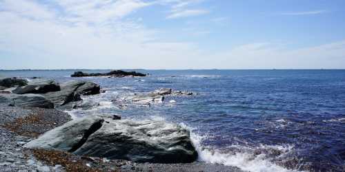 A serene coastal scene with rocky shores and gentle waves under a clear blue sky.