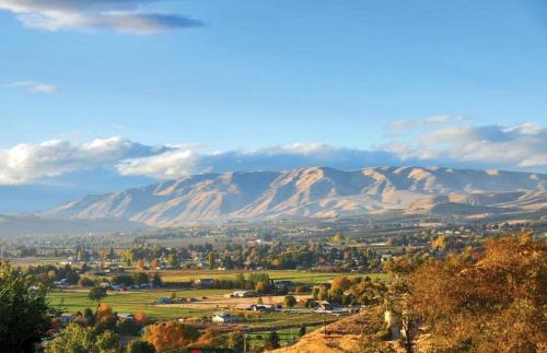 A scenic view of rolling hills and mountains under a blue sky, with lush green fields and trees in the foreground.