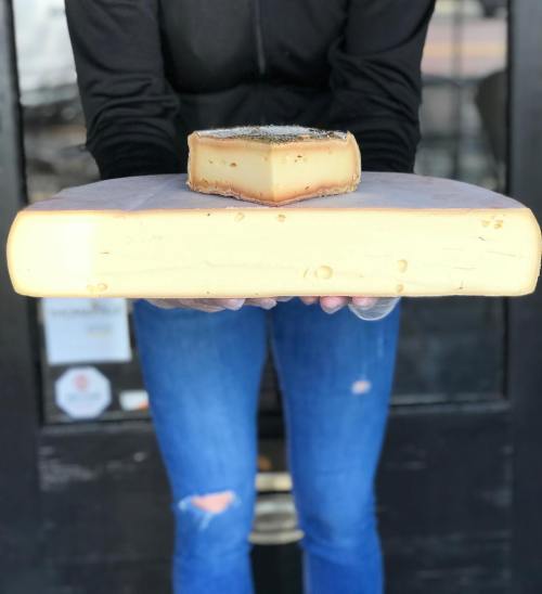 A person holds a large block of cheese with a smaller piece on top, set against a dark background.
