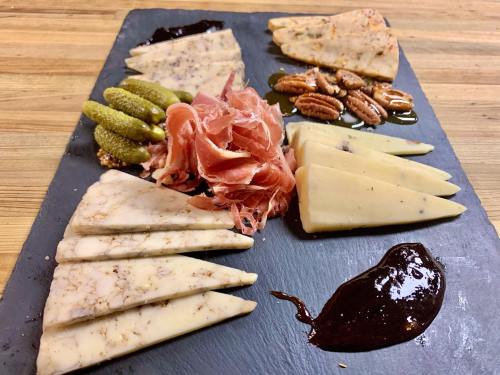 A charcuterie board featuring assorted cheeses, prosciutto, pickles, nuts, and a dark sauce on a slate platter.