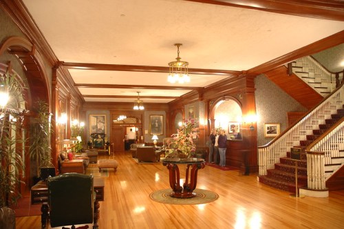 Elegant lobby with wooden accents, a staircase, and seating areas, featuring plants and decorative lighting.
