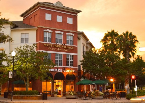 Sunset view of West Park Village luxury apartments with a Starbucks coffee shop at the base, surrounded by palm trees.