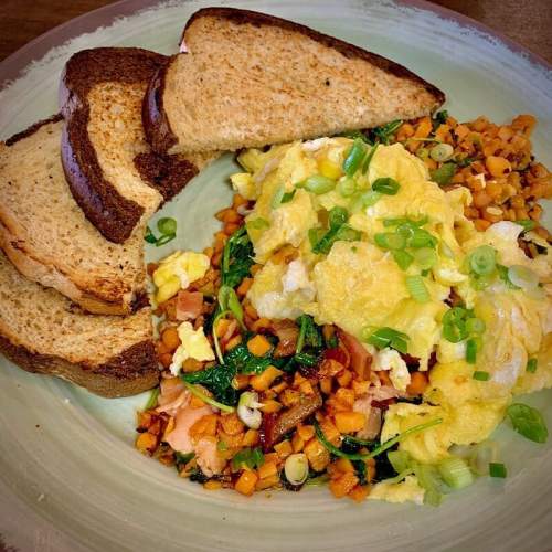 A plate with scrambled eggs, sautéed vegetables, and three slices of toasted bread.