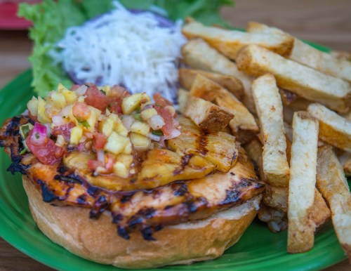 Grilled chicken sandwich topped with pineapple salsa, served with lettuce, shredded cabbage, and crispy fries.