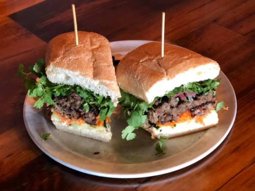 Two sandwiches on a plate, filled with a beef patty, fresh cilantro, onions, and shredded carrots, held together with toothpicks.