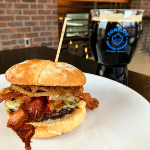 A delicious burger with bacon, cheese, and toppings, served with a dark beer in a cozy setting.