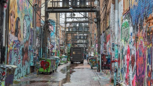 A vibrant alleyway filled with colorful graffiti, puddles on the ground, and a UPS truck in the distance.