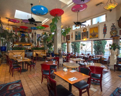 Colorful restaurant interior with vibrant umbrellas, plants, and artwork, featuring wooden tables and chairs.