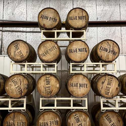 A stack of wooden barrels labeled "Blue Note" arranged on a white rack in a warehouse setting.