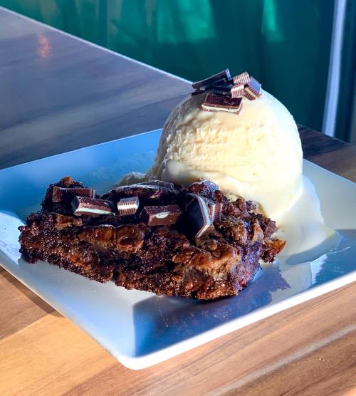 A decadent chocolate dessert topped with chocolate pieces, served with a scoop of vanilla ice cream on a white plate.