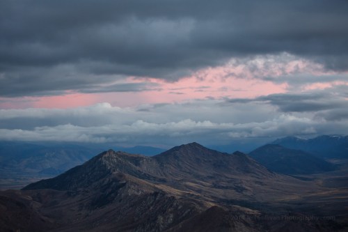 Dramatic mountain landscape under a cloudy sky, with hints of pink light on the horizon.