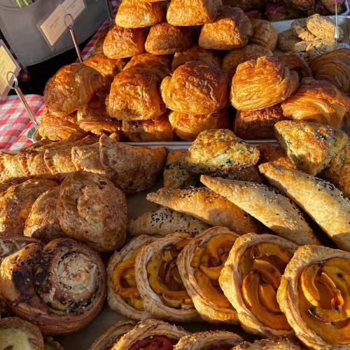 A variety of freshly baked pastries, including croissants, scones, and fruit tarts, displayed at a market.