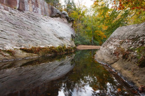 A serene landscape featuring a calm waterway reflecting rocky cliffs and vibrant autumn foliage.