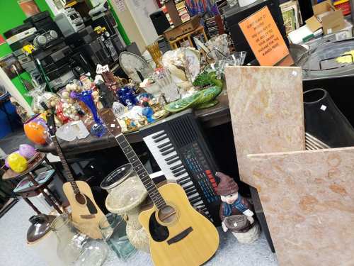 A cluttered table filled with various items, including guitars, glassware, and decorative objects in a thrift store.