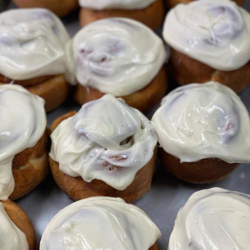 Freshly baked cinnamon rolls topped with creamy white frosting, arranged closely on a baking tray.