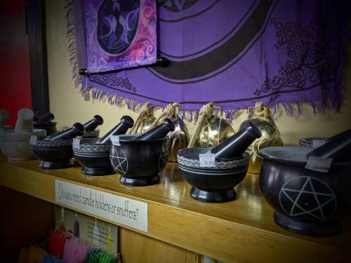 A display of black and silver mortar and pestle sets on a shelf, with colorful candles and a decorative tapestry in the background.