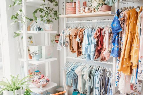 A cozy boutique display featuring colorful clothing on hangers and decorative plants on shelves.