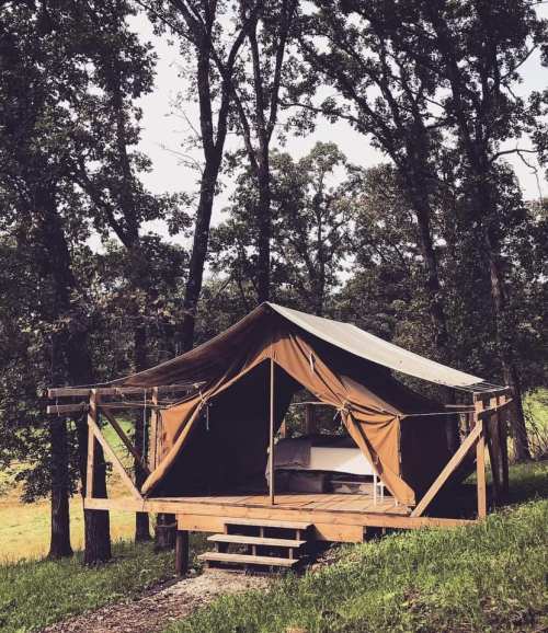 A canvas tent on a wooden platform surrounded by trees, set in a natural outdoor environment.