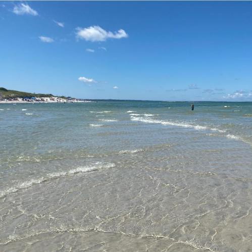A serene beach scene with clear water, gentle waves, and a blue sky dotted with clouds.