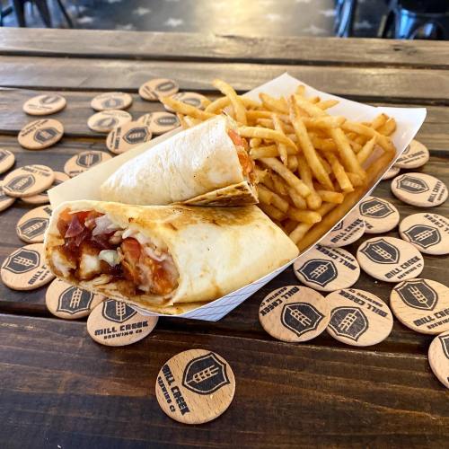 A wrapped burrito with bacon and a side of crispy fries on a wooden table with coasters.