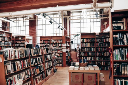 A cozy bookstore with wooden shelves filled with books and large windows letting in natural light.