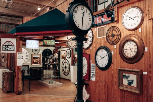 A display of various clocks on a wooden wall, featuring a large standing clock and framed artworks.