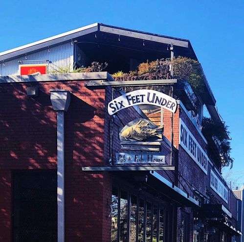 Sign for "Six Feet Under Pub & Fish House" on a brick building with a clear blue sky above.