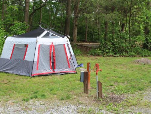 A large tent set up in a grassy area surrounded by trees, with two water spigots nearby.