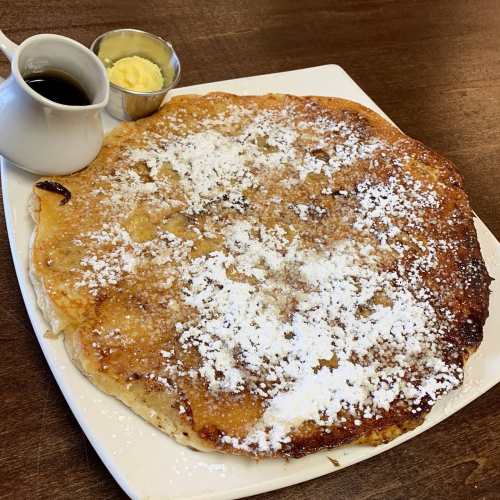 A large, golden pancake dusted with powdered sugar, served with butter and syrup on the side.