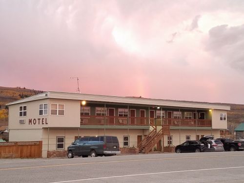 A two-story motel with a wooden balcony, parked cars in front, and a colorful sky in the background.