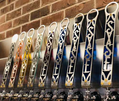 A row of colorful beer taps mounted on a brick wall, showcasing various designs and labels.