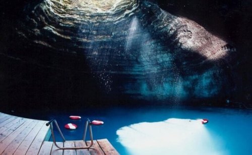 A serene underground pool with a wooden deck, illuminated by sunlight streaming through a circular opening above.