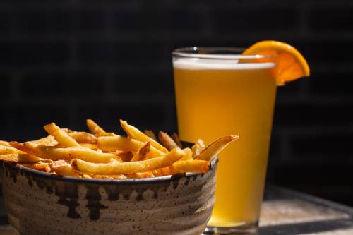 A bowl of golden French fries next to a tall glass of beer garnished with an orange slice.