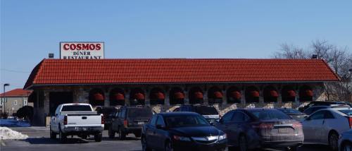 Exterior of Cosmos Diner Restaurant with a red-tiled roof and parked cars in front on a clear day.