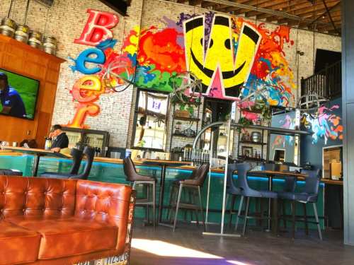 A vibrant bar interior featuring colorful graffiti, a cozy seating area, and a bartender at work.