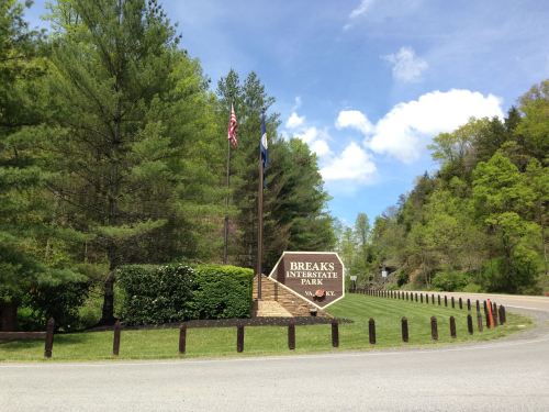 Sign for Breaks Interstate Park with flags, surrounded by greenery and a clear blue sky. Road visible in the foreground.