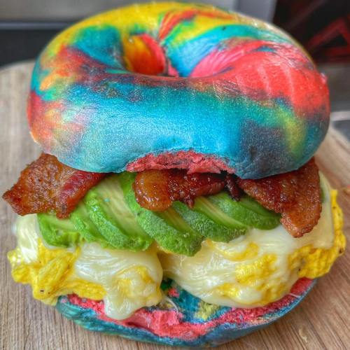 A colorful, tie-dye bagel sandwich filled with bacon, avocado, and scrambled eggs.