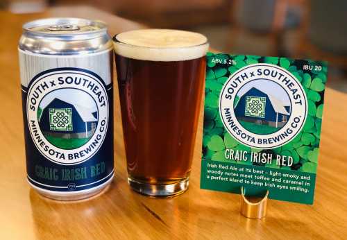 A can and glass of Craic Irish Red beer on a wooden table, with a sign detailing its ABV and IBU.