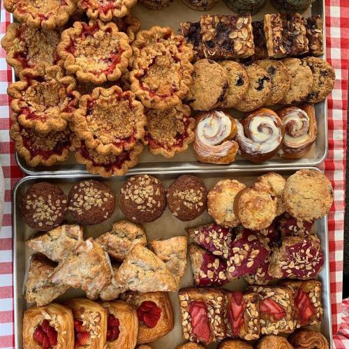 A variety of baked goods including pies, cookies, pastries, and muffins arranged on trays with a checkered background.