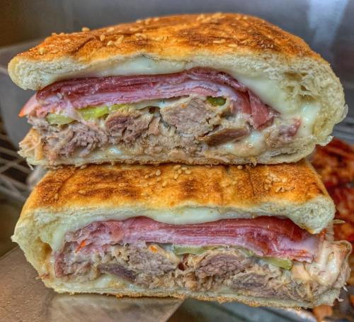 A close-up of a toasted sandwich filled with layers of meats, cheese, and pickles, showcasing a golden-brown crust.