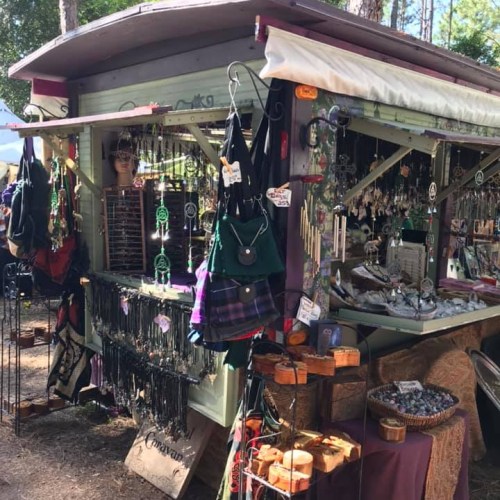 A colorful market stall filled with various handmade jewelry and crafts, set in a wooded outdoor area.