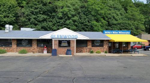 Exterior of a brick restaurant with a blue roof, sign reading "Glenwood," and a yellow patio area. Surrounded by greenery.