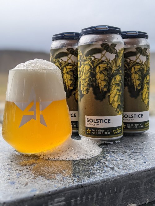 A frothy glass of Solstice Double IPA next to three cans, with hops illustrated on the can design.