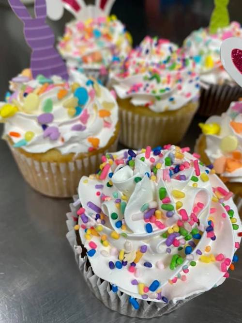 Colorful cupcakes topped with white frosting and vibrant sprinkles, decorated with playful bunny toppers.