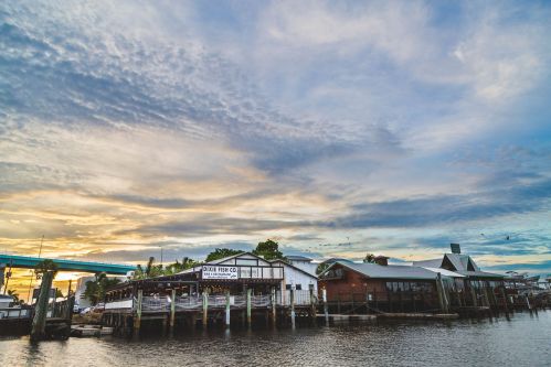 A waterfront scene featuring restaurants and a vibrant sky at sunset, reflecting on the calm water below.