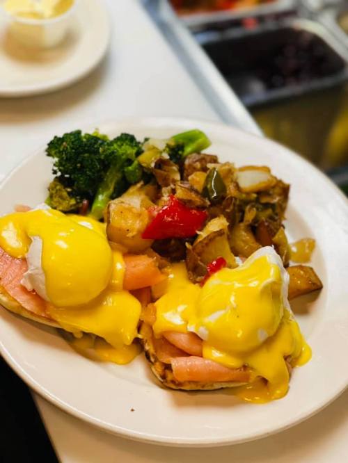 A plate of eggs Benedict with ham, topped with hollandaise sauce, served with broccoli and seasoned potatoes.